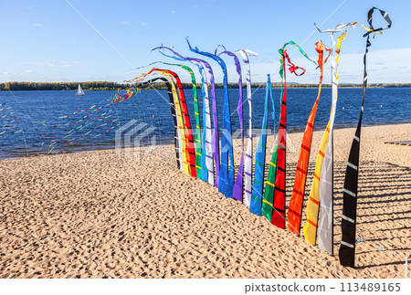 Decorative colorful flags fluttering on the sandy river bank on a sunny day Decorative colorful flags fluttering on the sandy river bank on a sunny day 113489165