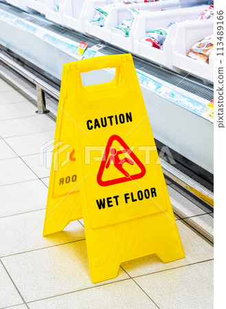 Caution Wet Floor yellow warning sign on a tile floor in a superstore Caution Wet Floor yellow warning sign on a tile floor in a superstore 113489166