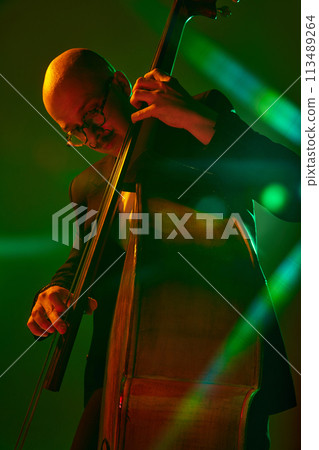 Talented musician playing jazz on double bass in red-green neon, stage light against gradient studio background. Talented musician playing jazz on double bass in red-green neon, stage light against gradient studio background. 113489264