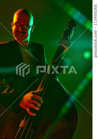 Contemporary double bass player in silhouette in red-green neon light against gradient studio background. Contemporary double bass player in silhouette in red-green neon light against gradient studio background. 113489268