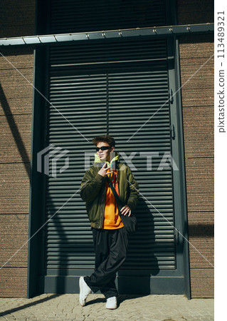 Modern portrait of trendsetting young attractive man, showcasing fusion of comfort and urban fashion standing near building. Modern portrait of trendsetting young attractive man, showcasing fusion of comfort and urban fashion standing near building. 113489321