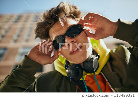 Creative portrait of young attractive guy, in trendy vibrant outfit and stylish, retro sunglasses posing against cityscapes. Creative portrait of young attractive guy, in trendy vibrant outfit and stylish, retro sunglasses posing against cityscapes. 113489351