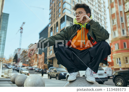 Trendy student exudes confidence, his oversized neon outfit reflecting vibrancy of modern youth culture and urban style. 113489373