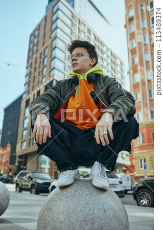 Young man poses against bustling cityscape, his neon over-size outfit bold statement of modern street fashion. Young man poses against bustling cityscape, his neon over-size outfit bold statement of modern street fashion. 113489374