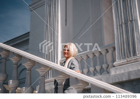 A woman is standing on a white staircase with a cup in her hand. She is smiling and looking up at the sky. A woman is standing on a white staircase with a cup in her hand. She is smiling and looking up at the sky. 113489396
