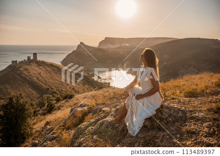 A woman in a white dress sits on a rock overlooking a body of water. The scene is serene and peaceful, with the woman enjoying the view and the calmness of the surroundings. A woman in a white dress sits on a rock overlooking a body of water. The scene is serene and peaceful, with the woman enjoying the view and the calmness of the surroundings. 113489397