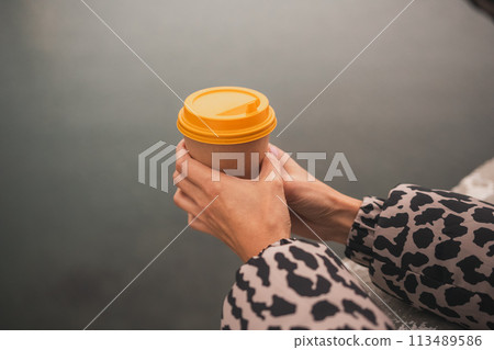 A person holding a coffee cup with a yellow lid. The person is wearing a leopard print jacket. A person holding a coffee cup with a yellow lid. The person is wearing a leopard print jacket. 113489586