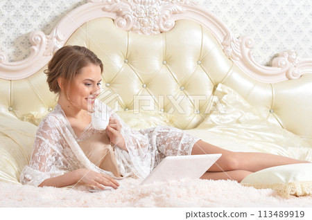 Portrait of young beautiful woman with coffee cup on bed 113489919