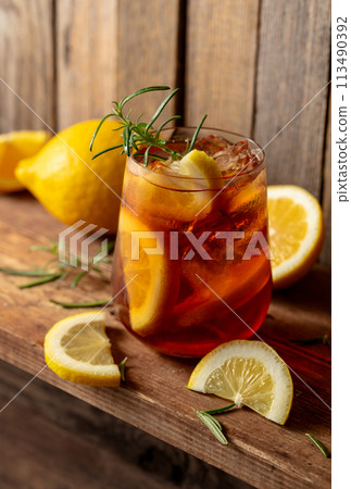 Iced tea or alcoholic cocktail with ice, rosemary and lemon slices on a old wooden table. 113490392