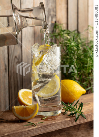 Water is poured from a decanter into a glass with ice and lemon slices. Water is poured from a decanter into a glass with ice and lemon slices. 113490393