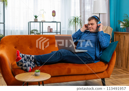 Happy relaxed man in wireless headphones sitting on home couch listening music in laptop netbook 113491957