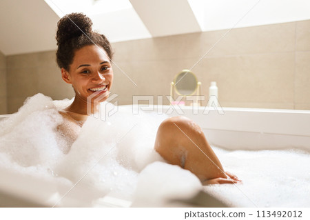 A woman smiles with comfort while bathing in a foamy bathtub 113492012
