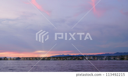 Twilight over a tranquil lake with city lights and pink-tinted clouds in the sky. Twilight over a tranquil lake with city lights and pink-tinted clouds in the sky. 113492215