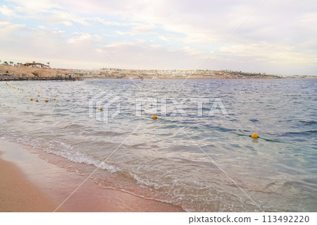 Scenic seaside view with calm waves, beach, and a coastal cityscape in the background. Scenic seaside view with calm waves, beach, and a coastal cityscape in the background. 113492220