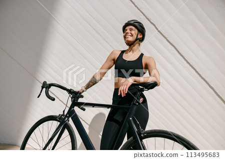 Professional female cyclist in protective gear looking at camera while riding bicycle in city center 113495683