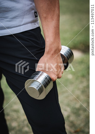一名 40 多歲的男子在公園裡用啞鈴進行肌力訓練 113497011