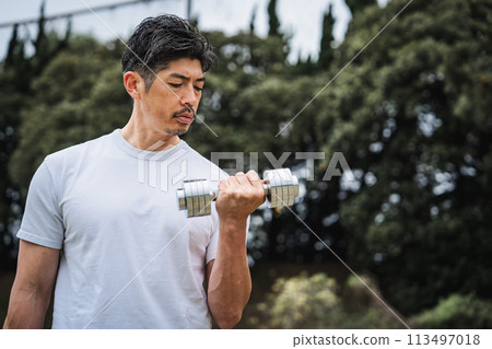 一名 40 多歲的男子在公園裡用啞鈴進行肌力訓練 一名 40 多歲的男子在公園裡用啞鈴進行肌力訓練 113497018