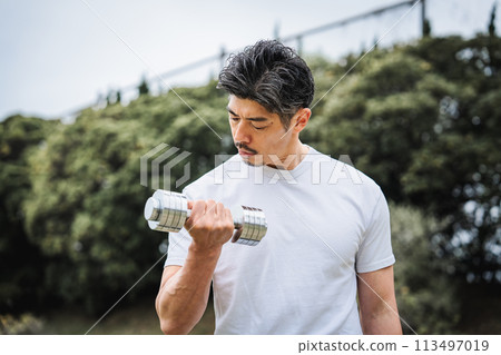 一名 40 多歲的男子在公園裡用啞鈴進行肌力訓練 113497019