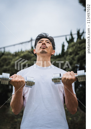A man in his 40s doing strength training with dumbbells in the park A man in his 40s doing strength training with dumbbells in the park 113497032