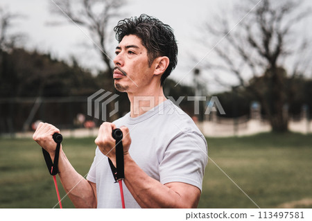 一名 40 多歲的男子在公園裡用訓練管進行肌肉訓練 113497581