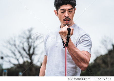 一名 40 多歲的男子在公園裡用訓練管進行肌肉訓練 一名 40 多歲的男子在公園裡用訓練管進行肌肉訓練 113497587