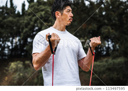 A man in his 40s doing muscle training with a training tube in the park A man in his 40s doing muscle training with a training tube in the park 113497595