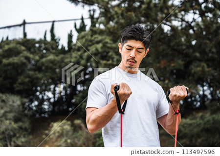 A man in his 40s doing muscle training with a training tube in the park A man in his 40s doing muscle training with a training tube in the park 113497596