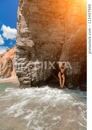 Woman swimsuit sea. Attractive blonde woman in a black swimsuit enjoying the sea air on the seashore around the rocks. Travel and vacation concept. Woman swimsuit sea. Attractive blonde woman in a black swimsuit enjoying the sea air on the seashore around the rocks. Travel and vacation concept. 113497999