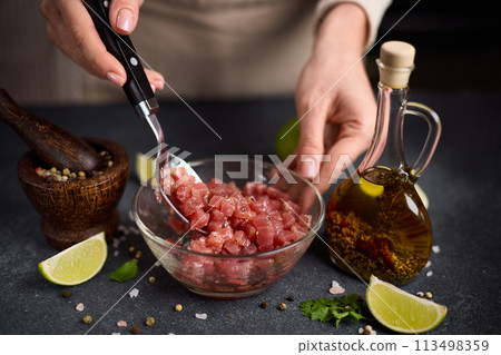 Woman mixing Sliced and chopped tuna fillet and spices in glass bowl cooking traditional tartare Woman mixing Sliced and chopped tuna fillet and spices in glass bowl cooking traditional tartare 113498359