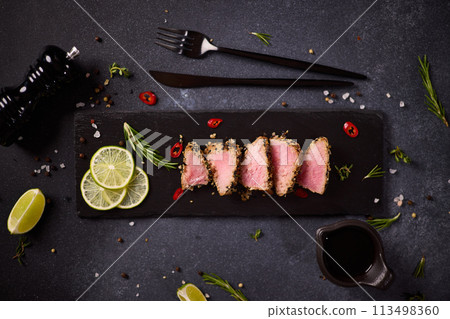 Sliced Organic grilled Tuna fillet covered with sesame seeds on black stone serving board Sliced Organic grilled Tuna fillet covered with sesame seeds on black stone serving board 113498360