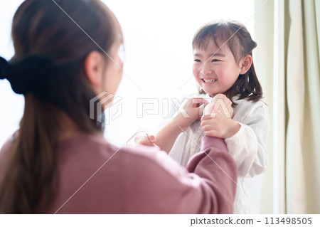 Mother helping little girl change clothes Mother helping little girl change clothes 113498505