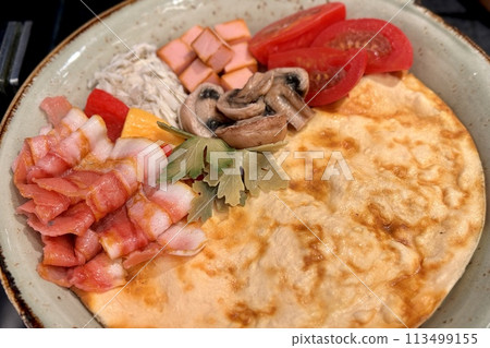 Scrambled eggs with bacon, mushrooms, tomatoes on a plate on a table. Close-up 113499155