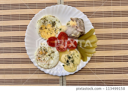 Round fried eggs with tomatoes on a white plate on a tablecloth. Close-up Round fried eggs with tomatoes on a white plate on a tablecloth. Close-up 113499158
