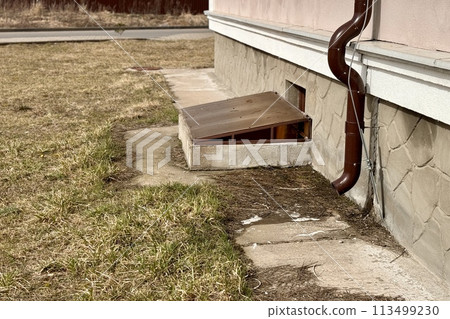 Brown stainless steel drain pipe for drain pipe with water drainage from roof the house to the ground. It attaches to a wall of residential building and leading to concrete surface 113499230