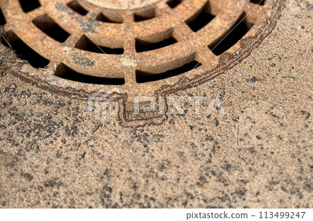 A rusty iron hatch with a pattern above an observation well is located on auto road in daytime. Close-up 113499247