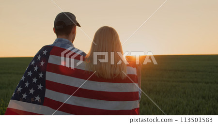 Two farmers with american flag on their shoulders looking forward in wheat field at sunset 113501583