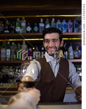 smiling bartender with classical metal shaker . Shelves with bottles of alcohol in background. smiling bartender with classical metal shaker . Shelves with bottles of alcohol in background. 113503341