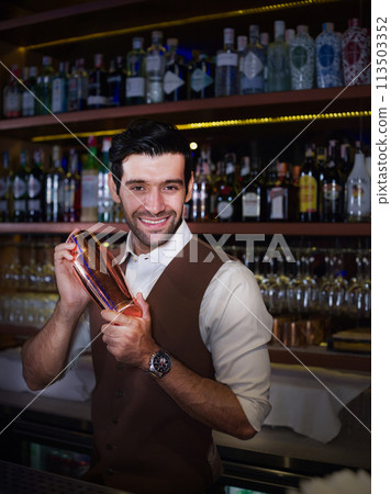 Handsome smiling bartender with shake classical metal serving drinks to people at party. Handsome smiling bartender with shake classical metal serving drinks to people at party. 113503352