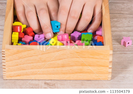 Hands of kid playing thread and colorful beads used to making bracelets Hands of kid playing thread and colorful beads used to making bracelets 113504379