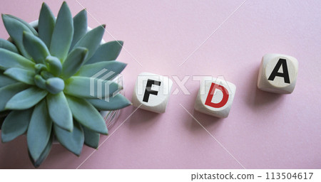 FDA - Food Drug Administration symbol. Wooden cubes with word FDA. Beautiful pink background with succulent plant. Medical and Food Drug Administration concept. Copy space. 113504617