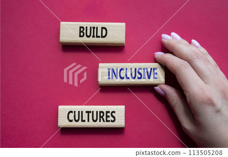 Build Inclusive Cultures symbol. Wooden blocks with words Build Inclusive Cultures. Beautiful red background. Businessman hand. Business and Build Inclusive Cultures. Copy space. 113505208