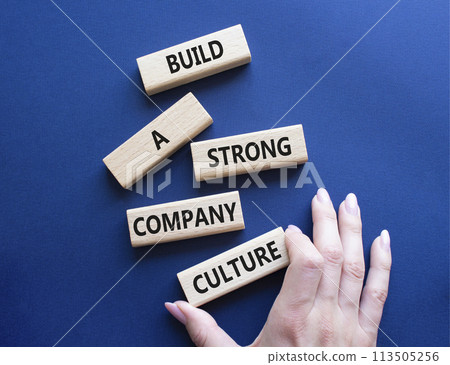 Company culture symbol. Wooden blocks with words Build a strong company culture. Beautiful deep blue background. Businessman hand. Business and Company culture concept. Copy space. Company culture symbol. Wooden blocks with words Build a strong company culture. Beautiful deep blue background. Businessman hand. Business and Company culture concept. Copy space. 113505256