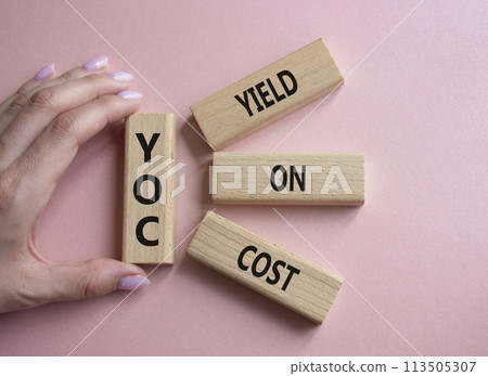 YOC - Yield on Cost. Wooden cubes with word YOC. Businessman hand. Beautiful pink background. Business and YOC concept. Copy space. YOC - Yield on Cost. Wooden cubes with word YOC. Businessman hand. Beautiful pink background. Business and YOC concept. Copy space. 113505307