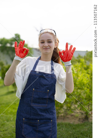 Front view of girl, florist working in garden, showing alright, smiling. Concept of taking care of nature. Front view of girl, florist working in garden, showing alright, smiling. Concept of taking care of nature. 113507162