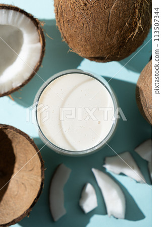 Coconut milk in a glass among coconuts on a blue background top view 113507344
