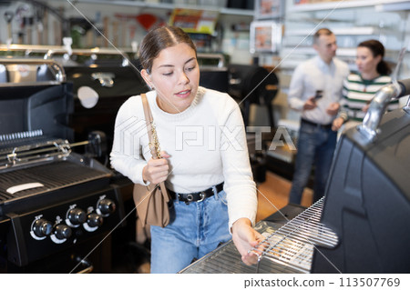 Young woman shopping at garden supermarket - choosing new grill for frying meat Young woman shopping at garden supermarket - choosing new grill for frying meat 113507769