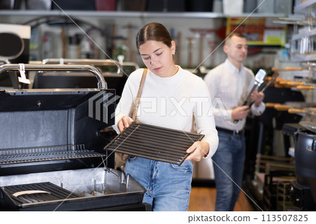 In store, girl inspects mobile grill, buys barbecue device 113507825
