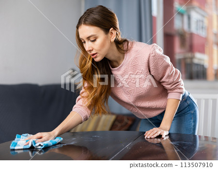 Young woman cleans table at home 113507910