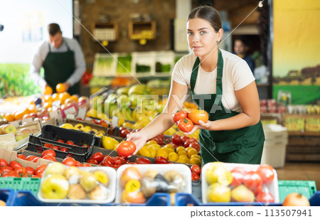 Young female seller wearing apron holding fresh tomatoes on market 113507941