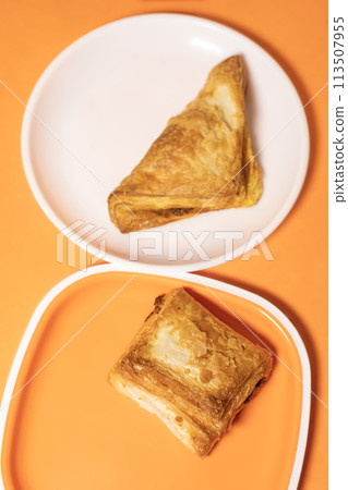 Two pieces of veg puff pastry on a plate on an orange background. Top view 113507955